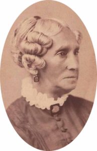 A portrait of Sarah Harris Fayerweather in her older age. She is wearing a high collared dress and her hair is styled in a fancy updo. The photo is in sepia tone, making the image in shades of brown/tan.