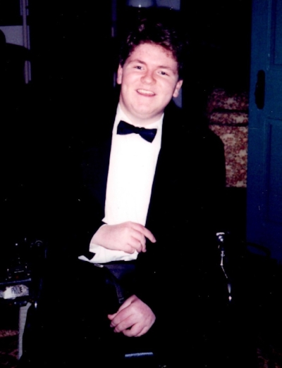 Jim sits in tux. His bright smile lights up the photo as he looks past the photographer at something on his right.