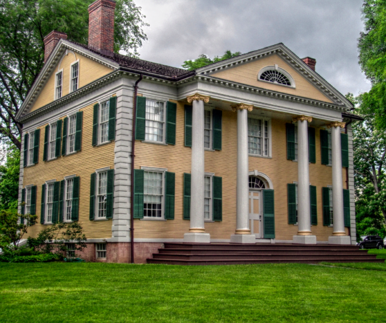 A beautiful yellow brick building with white columns and black shutters.