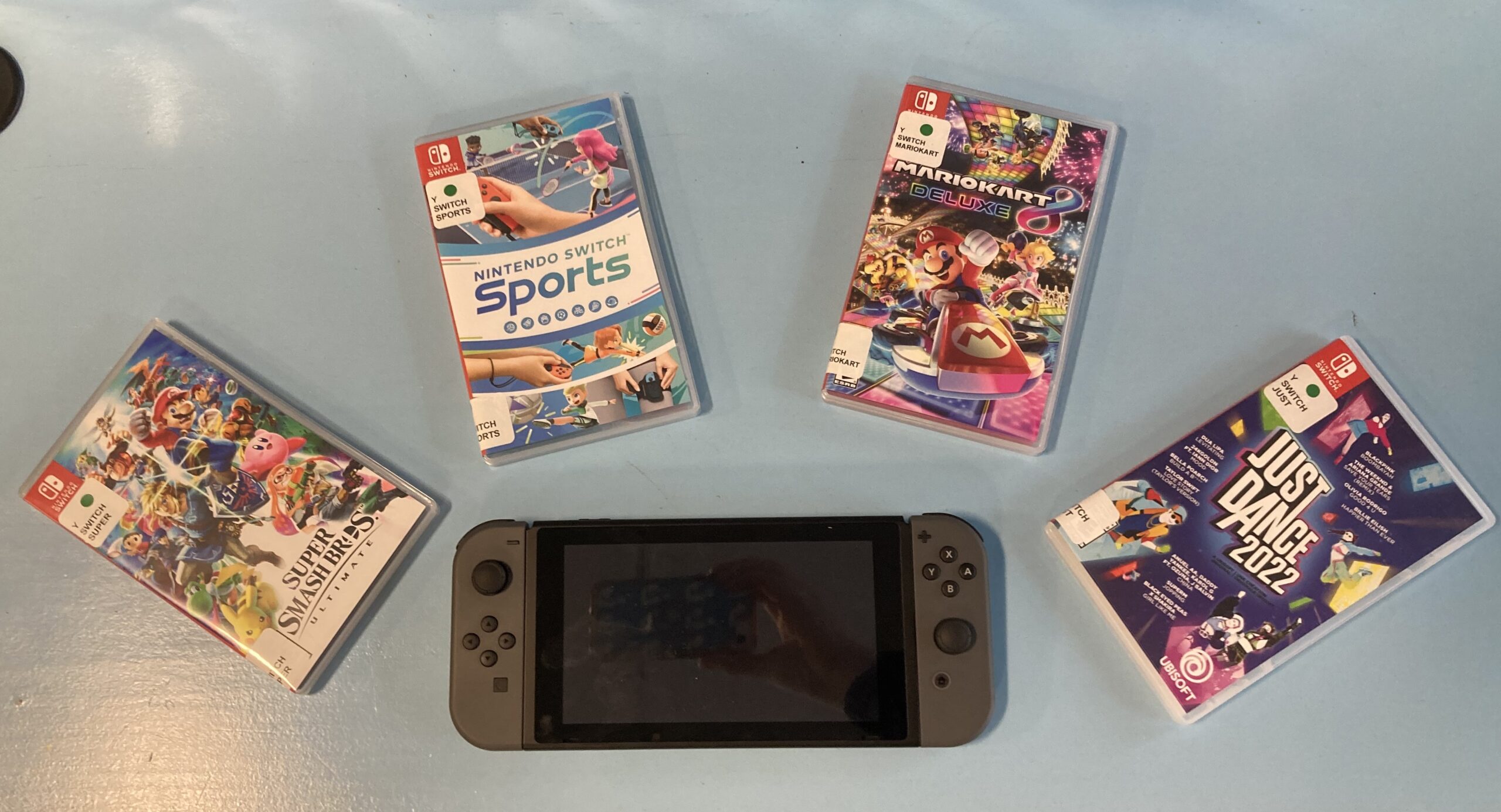 A black Nintendo Switch lies against a blue table. Fanned out around it are various games, including Just Dance and Mario Kart.