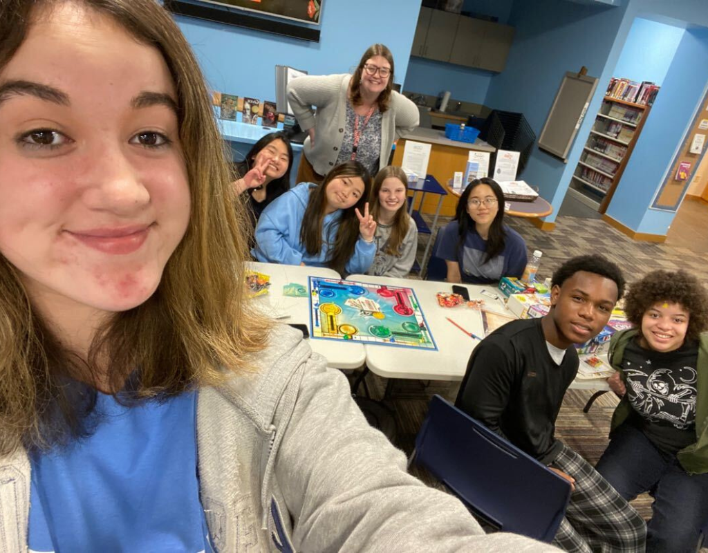 A group of teens at YA Game Night posing with Kait, the librarian