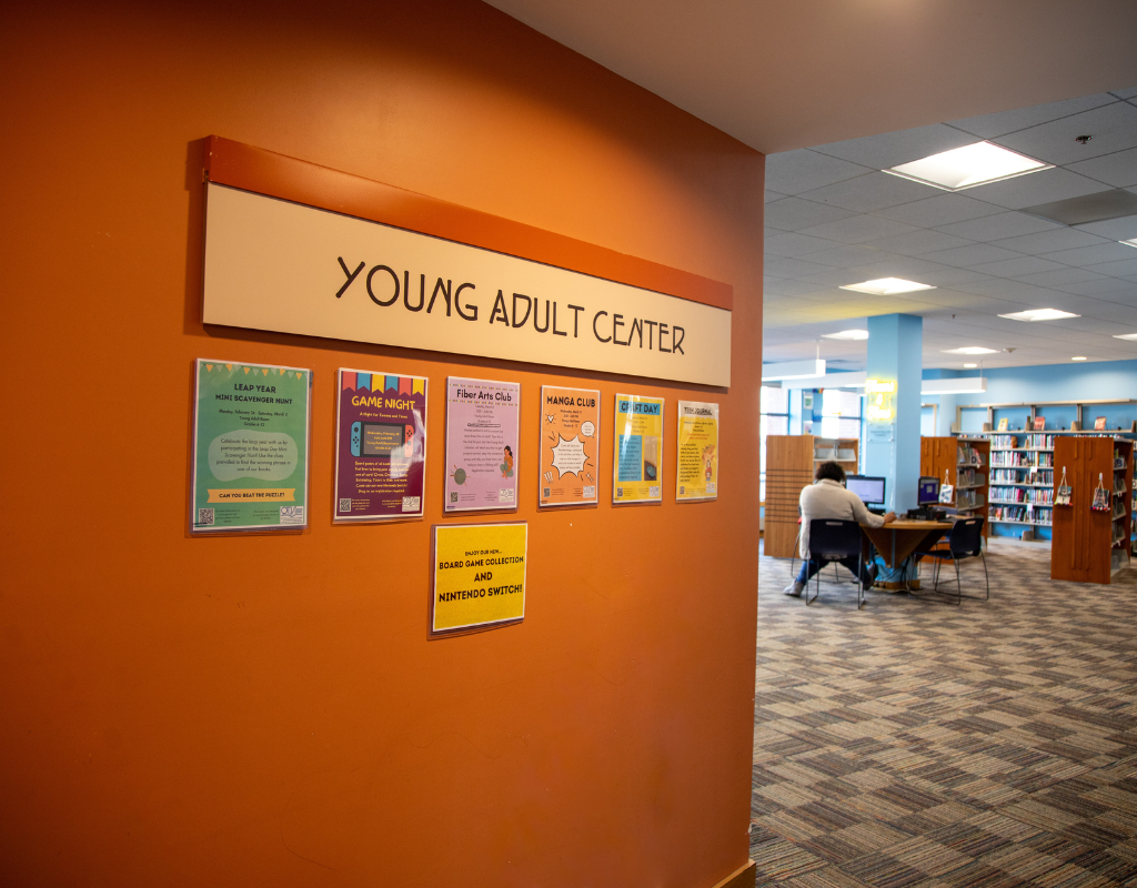 YA sign against the orange wall with flyers for teen events underneath