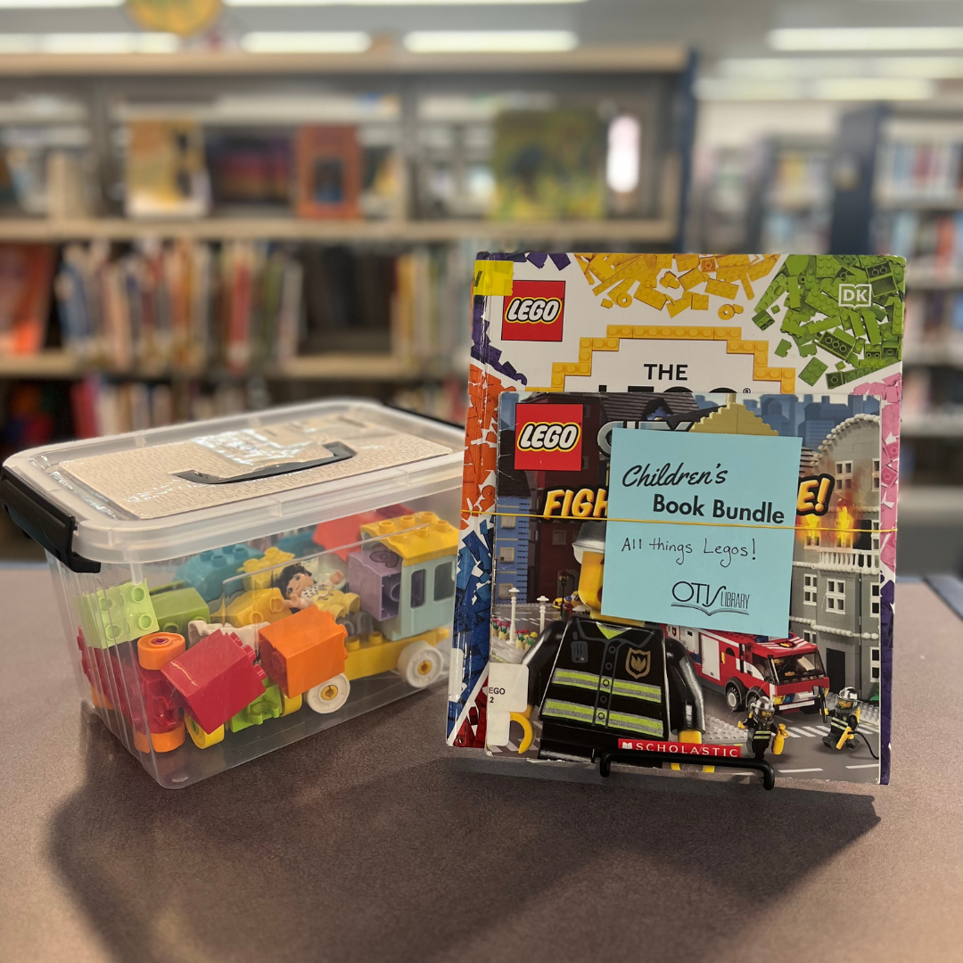 A bin of LEGO sits next to a book about LEGO. Taped to the book is a blue card identifying the pair as a Book Bundle themed after the popular toy.